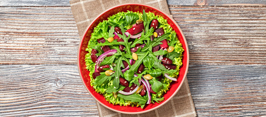 Vegan beetroot salad with red bean, lettuce, arugula, seed. Home made vegetarian beet salad on wood background. Tasty fresh summer beetroot veg dish. Top view.