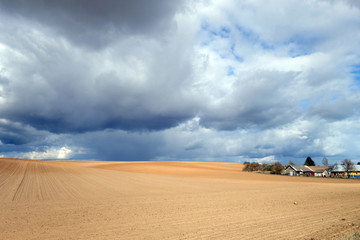 Cultivated agricultural field and sky with clouds. Village nearby