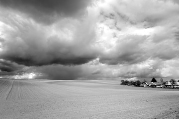 Cultivated agricultural field and sky with clouds. Black and white