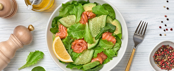 Salmon salad, cucumber, spinach, lollo, lettuce. Homemade vegetarian salmon salad. Seafood creative diet concept. Summer salmon salad on white wood, closeup, banner