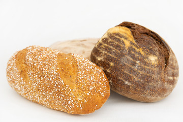 Three crunchy breads made of wheat and rye flour. Fresh loafs baking at home isolated on white background. Studio shot. Selective focus. Side view. Homemade food and nutrition concept