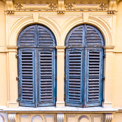 Alte gelbe Fassade und zwei Fenster mit blauen Holz Fensterläden als Hintergrund