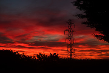 Naklejka premium An electricity pylon, also said transmission tower, stands in the countryside of Somerset, England. The sky is on fire right after sunset.