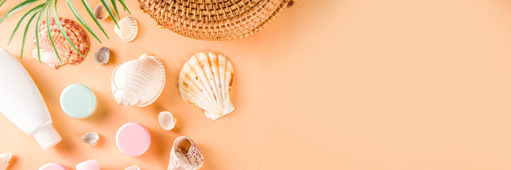 Summer cosmetics background. Summer skincare, sunscreen cosmetics, travel kit miniatures flat lay. Trendy peach background, with women bag, sea shells, tropical leaves, straw hat. Copy space above