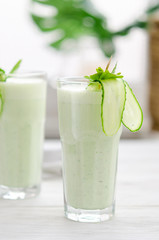 Refreshing fermented milk drink with cucumber and herbs. Two with such a cocktail in a light interior on a white table.