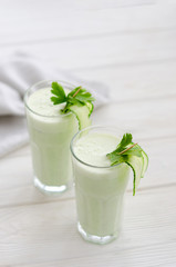 Refreshing fermented milk drink with cucumber and herbs. Two with such a cocktail in a light interior on a white table.