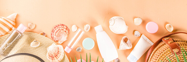 Summer cosmetics background. Summer skincare, sunscreen cosmetics, travel kit miniatures flat lay. Trendy peach background, with women bag, sea shells, tropical leaves, straw hat. Copy space above