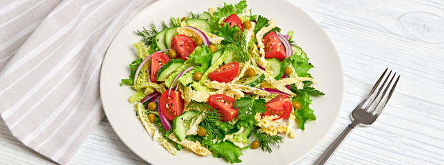 Savoy cabbage salad with cherry tomatoes, cucumeber on dish. Healthy summer salad vegetarian meal concept. Mixed leaves, tomatoes and vegetable salad on white wood, banner
