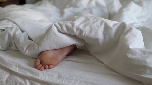 Woman sleeping in bed under white blanket, female feet sticking out from under duvet in bed.