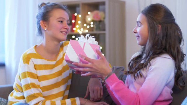 people, friendship and holidays concept - happy teenage girl giving present to her friend at home