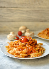 Pasta in a white plate. Pasta with cherry tomatoes and mushrooms. Light background. Free space for text. Vertical view