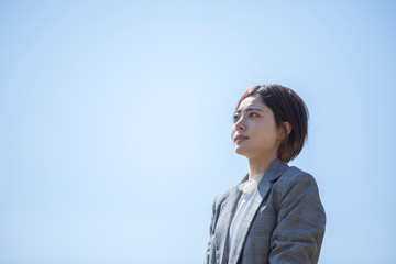 青空を背景に佇むスーツを着た若いビジネスウーマン