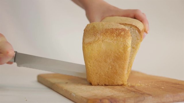 A woman cuts a loaf of white bread with a knife. 50p