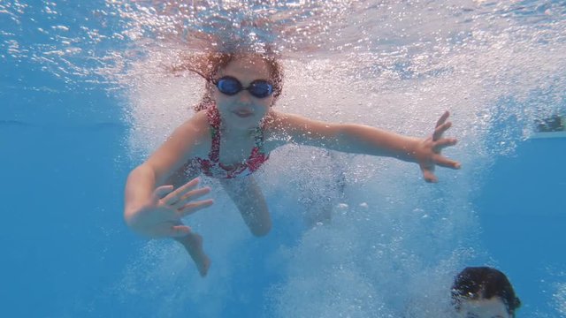 Children enjoying summer vacation. Happy fun loving group of friends jumping and diving into swimming pool at a pool party in summer sunny day. Slow motion. Underwater view