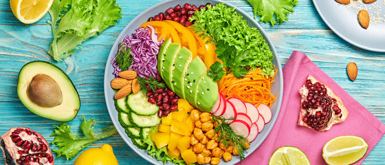 Buddha bowl salad with avocado, tomato, lettuce, cucumber, red cabbage, chickpeas, pomegranate. Vegan and balanced salad concept. Rainbow mix summer salad on wood, banner