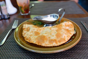Juicy cheburek with sour cream. Crimean Tatar cuisine. Meat pie.