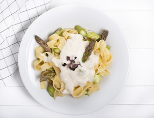 Fresh homemade pasta dish of fettuccine or tagliatelle, green asparagus, white sauce, white plate