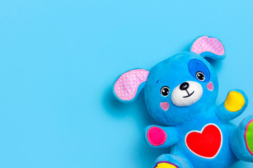 Blue soft children's toy puppy with funny ears, multi-colored paws and red heart on blue background flat lay top view copy space. Plush toy dog, baby friend, children's play item, happy childhood