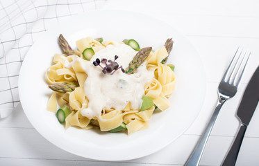 Fresh homemade pasta dish of fettuccine or tagliatelle, green asparagus, white sauce, white plate
