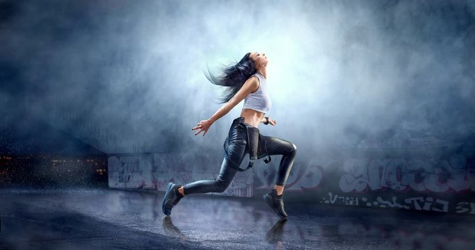 Female street dancer in a action with a graffity wall behind the fog on a backgroung.