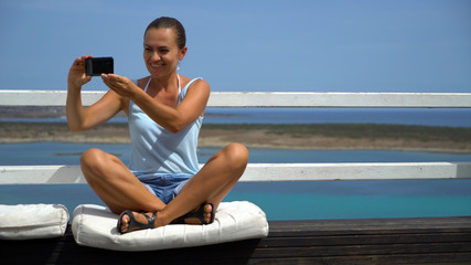 Fototapeta na wymiar Young tourist woman shooting selfie with smartphone over the sea, Sardinia, Italy 