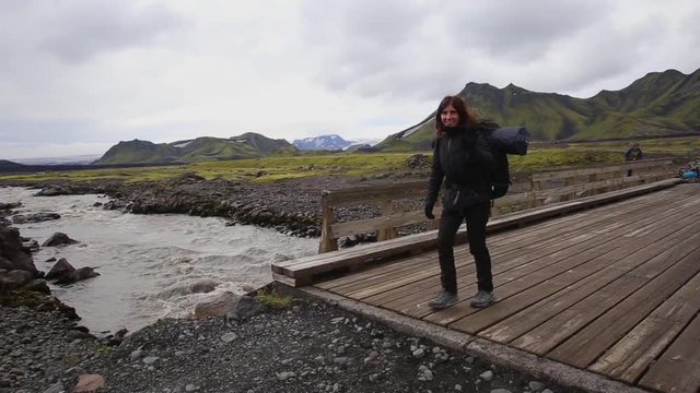A young woman with a backpack crossing a wooden bridge on the 54 km trek from Landmannalaugar, Iceland