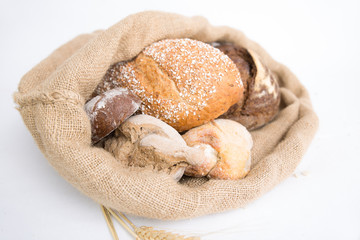 Traditional crusty loafs and buns in rustic burlap sack and wheat ears. Closeup shot. Isolated object on white background. Baking or homemade bread concept