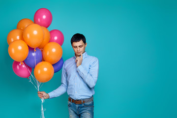 caucasian man in shirt with bright colorful balloons thinking about somethinh isolated on blue background.