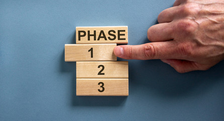 Wooden blocks form the words 'phase, 1, 2, 3,' on blue background. Male hand. Beautiful background.