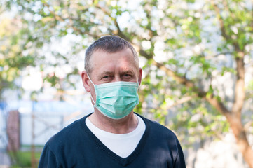 Portrait of mid age european man with surgery face mask on backyard background in sunny spring day