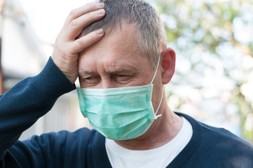 Portrait of middle aged european man has headache in surgery face mask on backyard background in sunny spring day