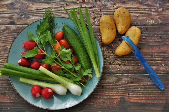 fresh vegetables on a blue plate and potatoes on a wooden brown table