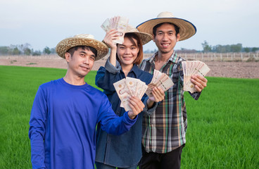 Group of three asian farmers smile and holding Thai banknote standing at rice farm. Small business concept