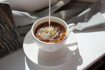 A trickle of milk pours into black coffee