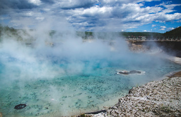 Aquamarine blue pool with huge steam in Yellowstone National Park United States. Nature concept with geysers, travel wallpaper from the most famous landmark with incredible basin color.