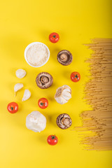 Spaghetti pasta with ingredients for cooking pasta on a yellow background. Colorful top and closeup