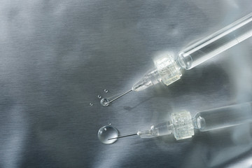 close-up of two syringes with a Luer lock with needles and drops of injections leaking on a silver...