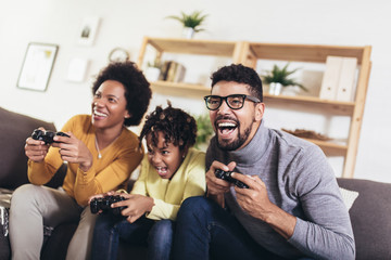 African American family at home sitting in sofa couch and playing console video games together