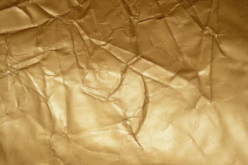 Texture of golden crumpled paper. Background fabric of gold color, creases. Crumpled gold-plated gift wrapping paper.