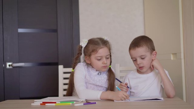 Sister helps little brother to draw. Two caucasian children drawing a picture together. An older sister helps her little brother with the art of drawing.