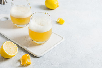 Two whiskey sour cocktails with ingredients, lemon juice, sugar syrup and egg white in glass on white. Horizontal orientation. Close up. Space for text.