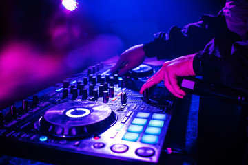 Fototapeta na wymiar DJ console for mixing music with hands and with blurred people dancing at a night club party