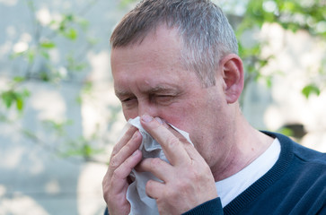 Portrait of middle aged european man blow nose on backyard background in sunny spring day