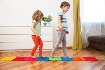 Two kids of presschool children walk on an massaging mat at home. prevention flat feet and hallux valgus.