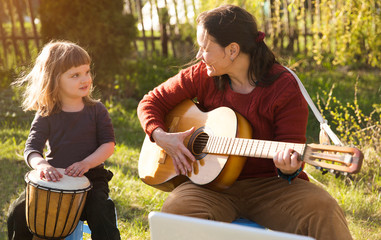 Happy family mom and child daughter having fun with musical instruments also sing songs together...