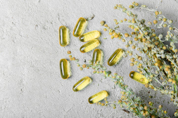 Omega-3 (fish oil capsules) and dry flowers on a gray concrete background. The concept of strengthening health and immunity with vitamins.