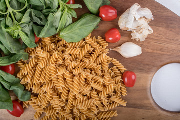 Gluten-free penne pasta from chickpeas, red lentils on wooden cutting board. basil,tomatoes, garlic