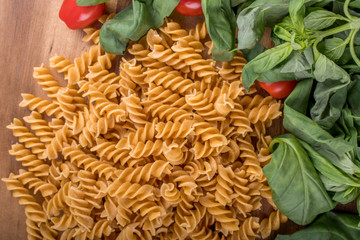 Gluten-free penne pasta from chickpeas, red lentils on wooden cutting board. basil,tomatoes, garlic
