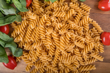 Gluten-free penne pasta from chickpeas, red lentils on wooden cutting board. basil,tomatoes, garlic
