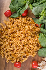 Gluten-free penne pasta from chickpeas, red lentils on wooden cutting board. basil,tomatoes, garlic